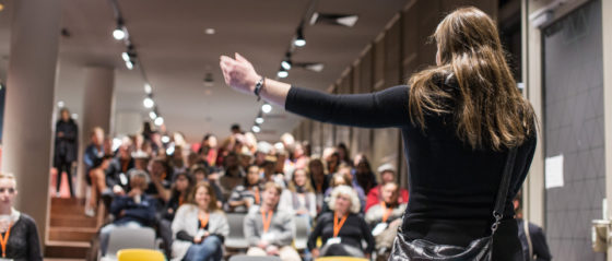 Eine Frau von hinten, die vor einem Publikum.