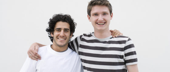 Zwei junge Männer legen sich die Hand auf die Schulter und lachen.