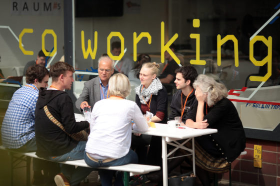 Eine Gruppe von sitzt draußen vor einem Co-Working Space und diskutiert.