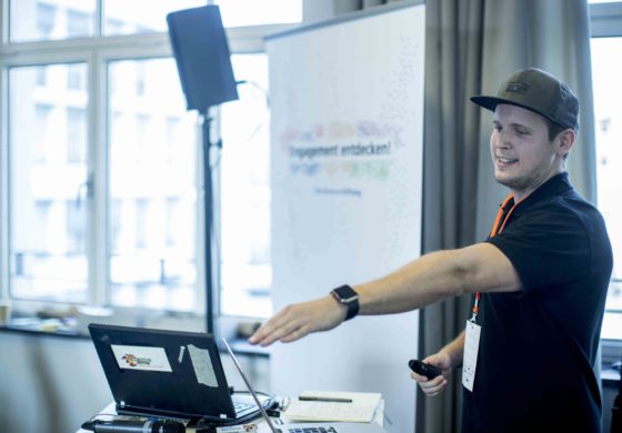 Ein junger Mann mit Basecap erläutert etwas am Laptop.