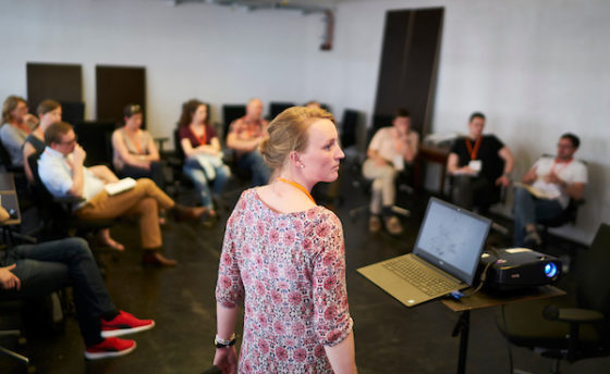 Eine Frau steht vor Menschen, die im Stuhlkreis sitzen.