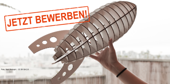 Eine Hand hält eine Rakete aus Holz in die Höhe.