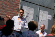 Ein Mann steht vor einer kleinen Menschenrunde und spricht.