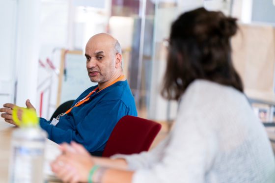 Ein Mann sitzt auf einem Stuhl, eine Frau hört zu.