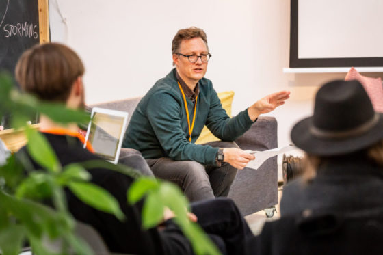 Ein Mann sitzt in einem Stuhlkreis und erklärt etwas.