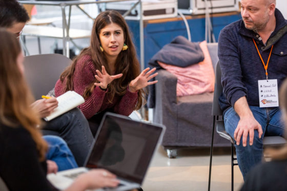 Eine Frau sitzt in einem Stuhlkreis und spricht gestikulierend.