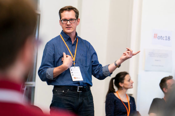 En Mann steht vor sitzenden Zuhörern und erklärt etwas.