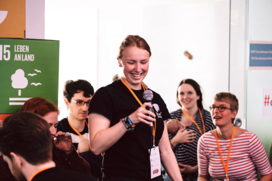 Eine Frau steht lachend mit einem Mikrofon zwischen weiteren Leuten.