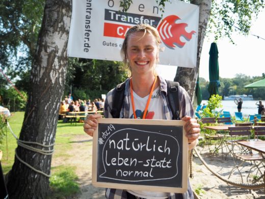 Ein junger Mann hält eine Tafel, auf der steht: natürlich leben statt normal