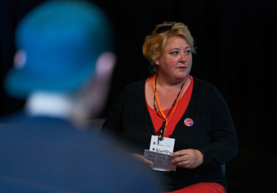 Eine Frau sitzt vor einer schwarzen Wand.