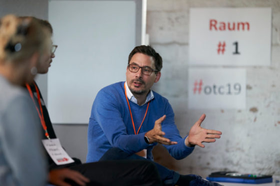 Ein Mann spricht zu zwei Zuhörern und gestikuliert.