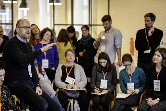 Ein Mann sitzt in einem Stuhlkreis und erklärt etwas.