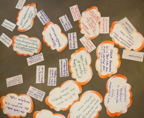 Mehrere beschriftete Post-its kleben auf einer braunen Fläche.